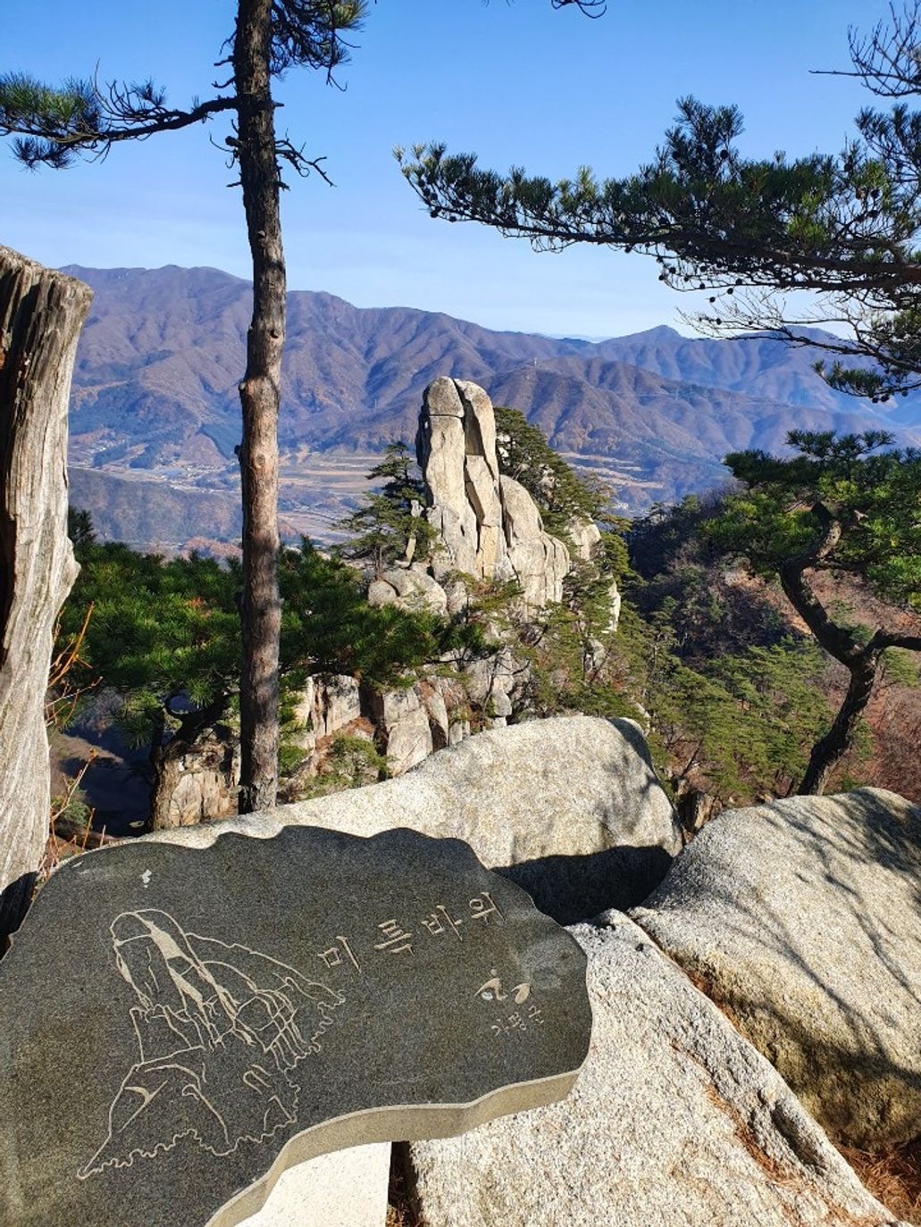 미륵바위 표지석과 그 뒤로 보이는 바위, 멀리 겹겹의 산줄기